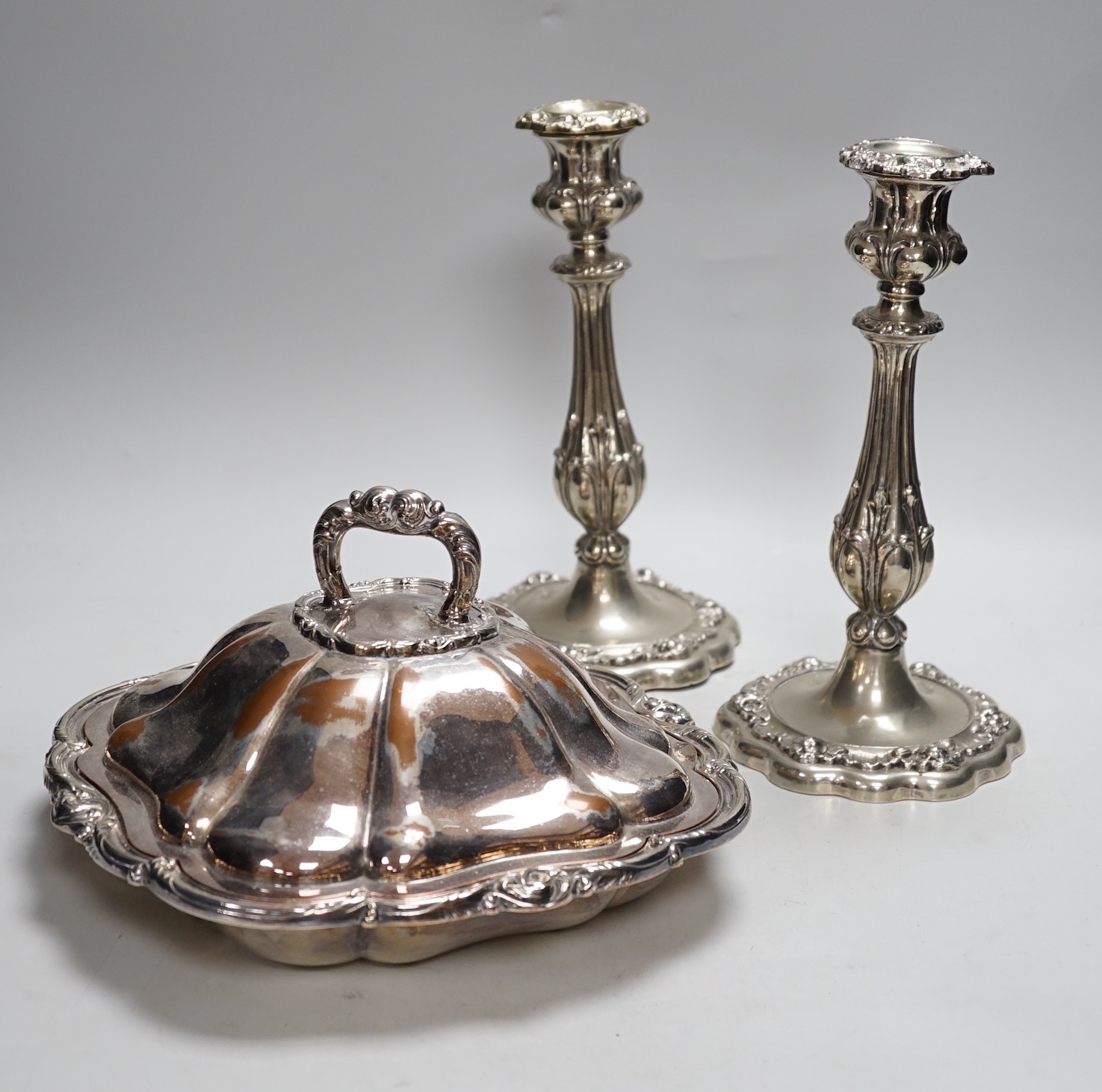 Three plated entree dishes and covers and a pair of candlesticks, candlesticks 26cm high